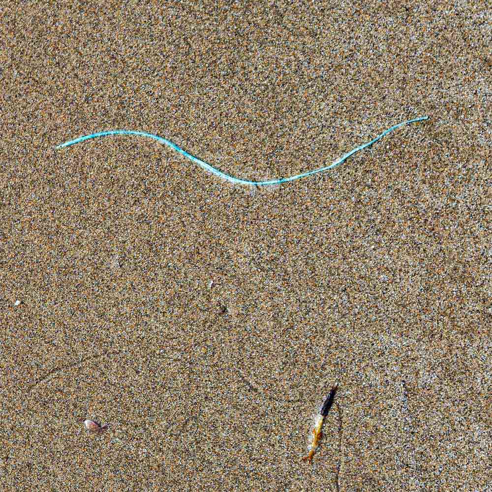 strands | A thin strand of cyan thread, sand and shadows on a Breton beach