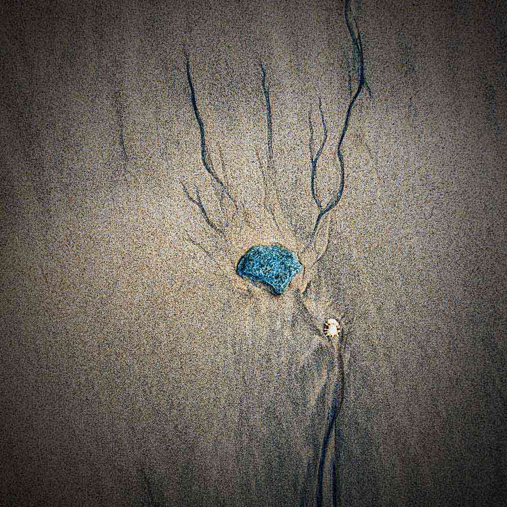 strands | A blue stone, cupped in a hollow in sand, and blue black manganese on a Breton beach