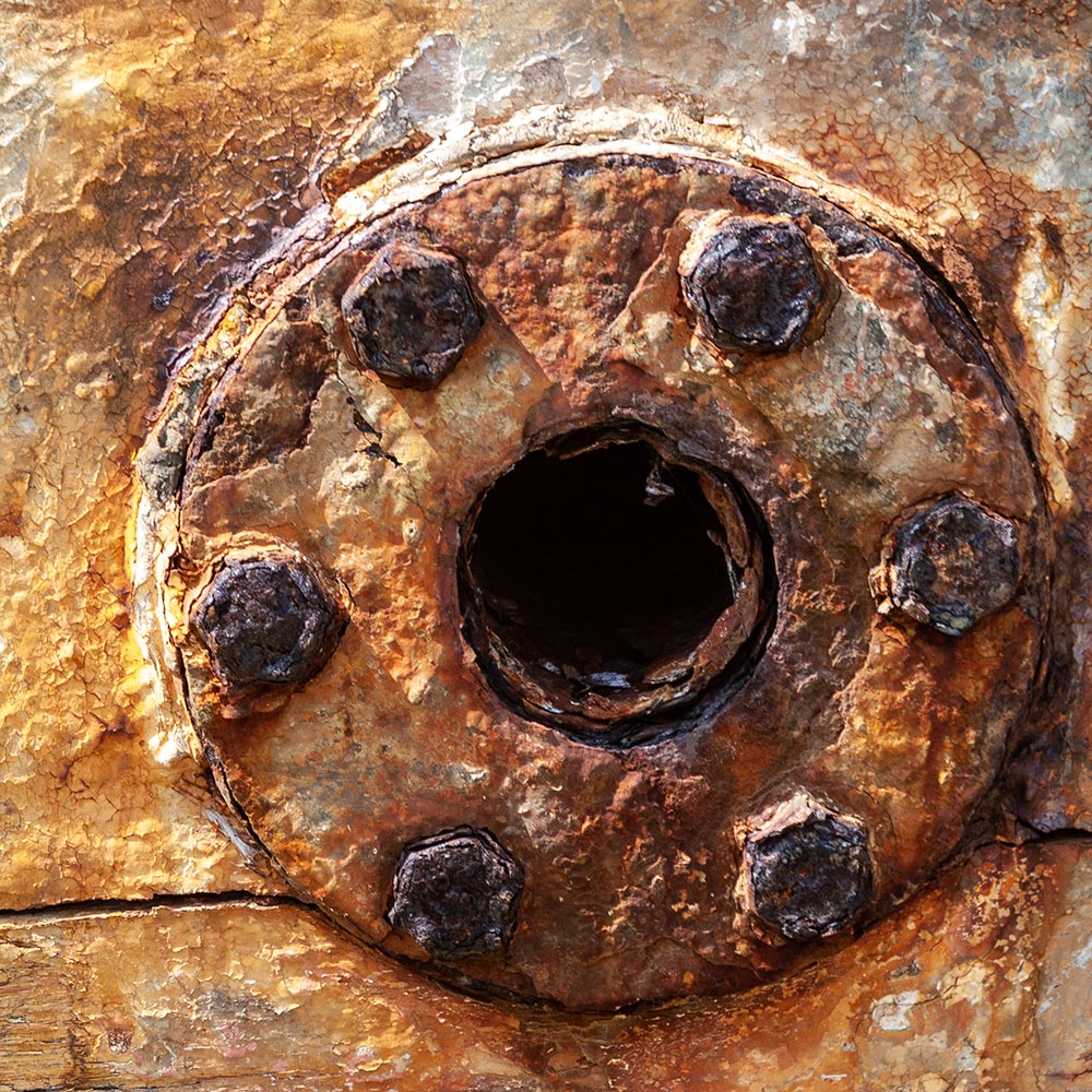 Camaret-sur_mer | a water waste pipe with peeling paint on the side of a rotting hulk of a fishing boat