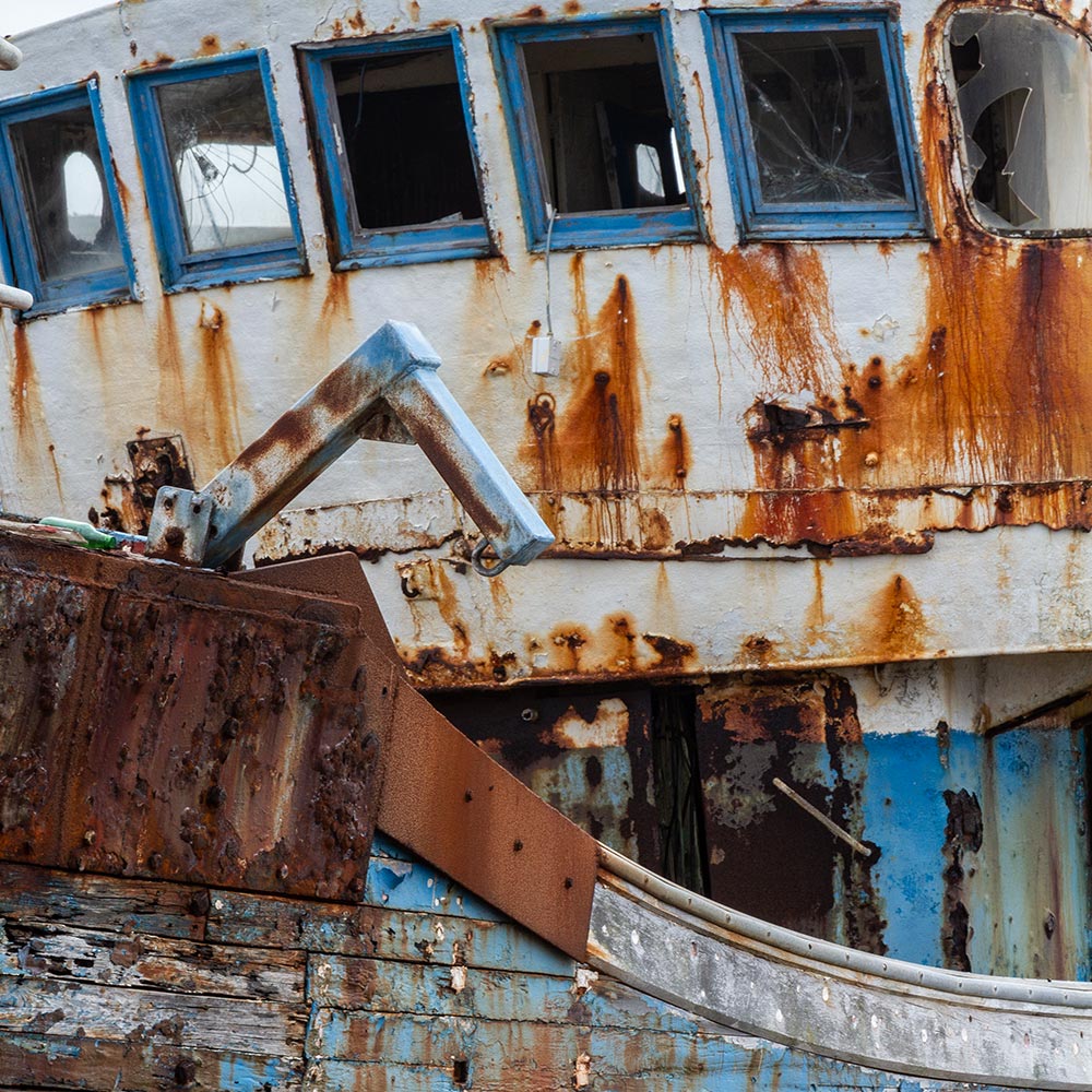 Camaret-sur_mer | a ships broken wheelhouse windows on the rusting superstructure of a rotting hulk of a fishing boat with rust marks on the paint