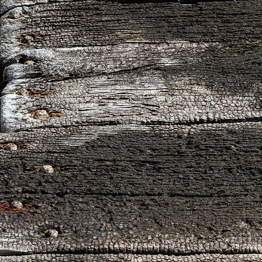 Camaret-sur_mer | The side of a burnt out rotting hulk of a fishing boat with peeling rusty white paint. Deeply textured worn panks of wood