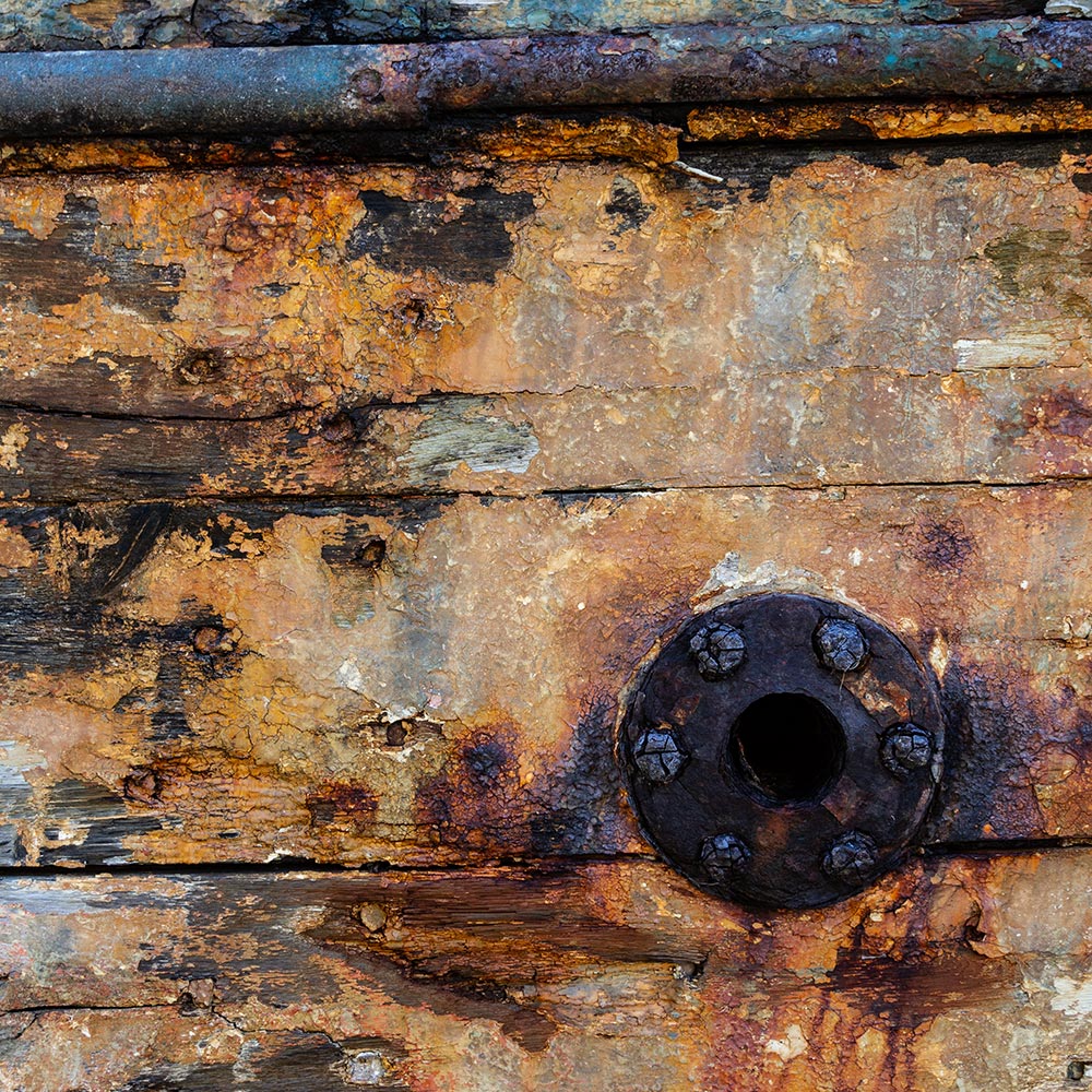 Camaret-sur_mer | The side of a rotting hulk of a fishing boat with peeling rusty green, blue and yellow paint